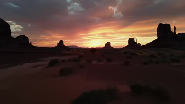 Sunset over desert landscape with monolithic rock formations and dramatic orange sky