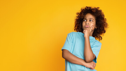 Let me think. Doubtful, thoughtful child girl posing over yellow background, copy space