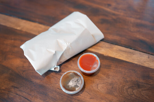 Bundle of fish and chips wrapped in white butchers paper on table with sauce and gravy - Powered by Adobe
