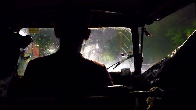 Cinematic footage of a tuk-tuk driving through heavy rain at night, with the driver silhouetted against glowing street and vehicle lights. 4K