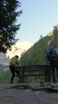 Vertical screen view of people walking by alpine lake with mountain peaks in background ouple walking near Lago di Braies with Dolomite mountains backdrop