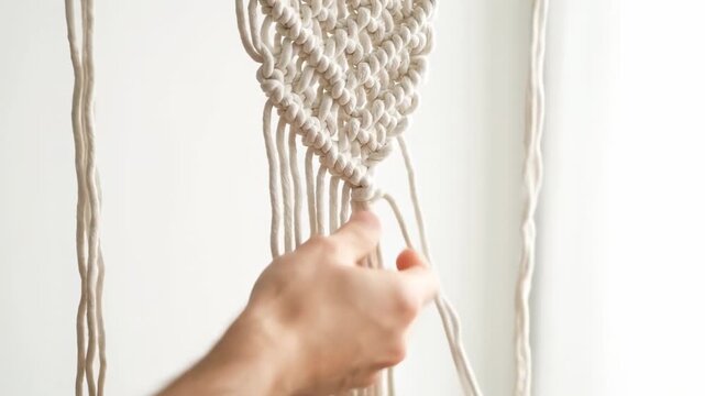 Close-up of hands creating macrame knotting with beige cord against a white background