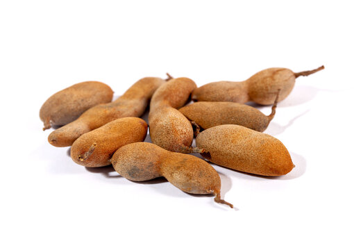 A pile of whole, ripe tamarind pods (Tamarindus indica) isolated on a white background. This tropical fruit is an essential ingredient in many Asian and Latin cuisines