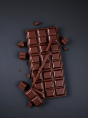 Dark chocolate bar with broken pieces displayed on a textured dark slate background