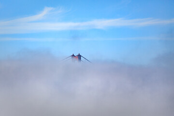 The Golden Gate Bridge is shrouded in fog, with only the top of the towers visible against a blue...