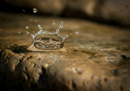 Water droplet impacts on a stone surface creating a crown like splash in a macro shot detailed and artistic