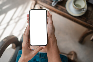 Hands holding a smartphone with a blank screen in a cafe, perfect for app or design mockups.