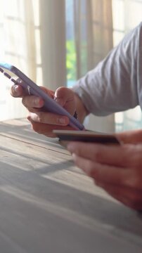 Asian man holds credit card and uses smartphone to pay for products online via the Internet.