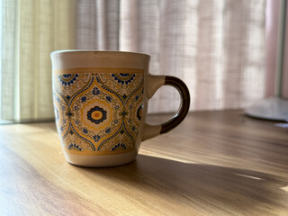 A yellow and blue cup with a floral design sits on a wooden table