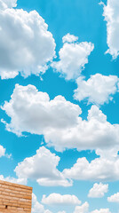 Bright blue sky with fluffy white clouds, peaceful atmosphere, and corner of brick wall in foreground, evoking sense of calm and openness