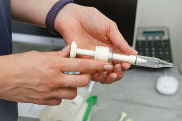 Close-up of audiologist hand preparing ear impression syringe for custom molded hearing aid or ear plug in clinic.