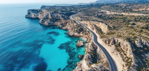 A drone shot of a winding coastal road hugging the cliffs, surrounded by turquoise waters and rugged rock formations.