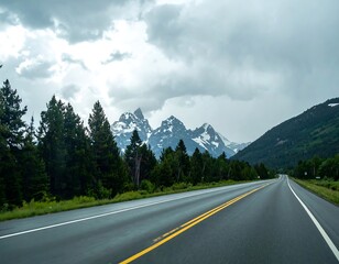 Fototapeta premium Scenic highway cuts through a valley, snow-capped mountains looming under a cloudy sky