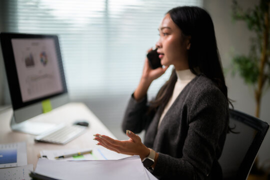 Asian businesswoman multitasking, talking on phone while working on computer