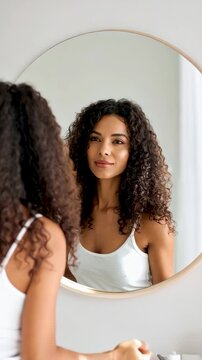 Mujer de cabello rizado mir&aacute;ndose al espejo en casa