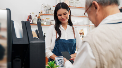 Asian senior male customer is paying for coffee through a mobile phone app to an Asian female barista coffee shop owner