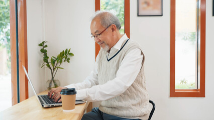 Asian senior man typing on computer laptop keyboard at coffee shop