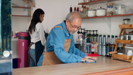 Asian senior owner man of a small coffee shop is cleaning the counter where he sells coffee