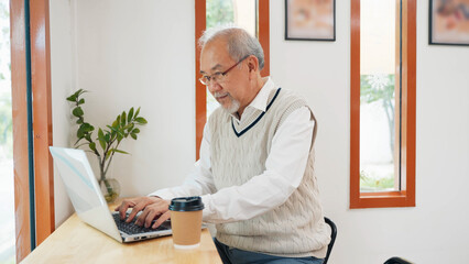 Asian senior man typing on computer laptop keyboard at coffee shop