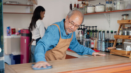 Asian senior owner man of a small coffee shop is cleaning the counter where he sells coffee