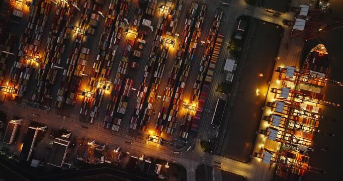Aerial shot of a large industrial container port with cranes and shipping containers stacked for import and export at night