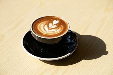 A cup of latte art coffee with a leaf design on a wooden table