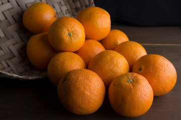 still life photography, Whole oranges falling from a woven basket onto a rustic wooden table on a black background, side view