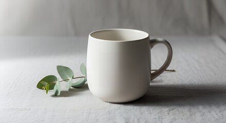 Minimalist white mug with eucalyptus branch on a textured linen surface