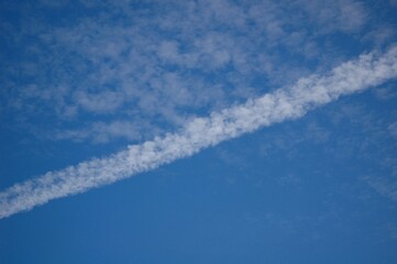 青い空に浮かぶかすれた雲と飛行機雲がほぐれた線のような雲が斜めに見える