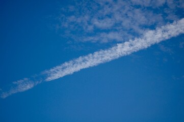 青い空に浮かぶかすれた雲と飛行機雲がほぐれた線のような雲が斜めに見える
