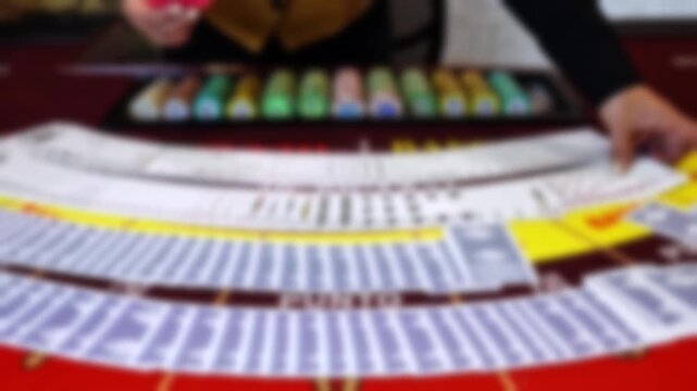 Defocused video of a baccarat table in a casino with cards spread across the table, colorful betting chips, and the dealer&rsquo;s hand in motion.