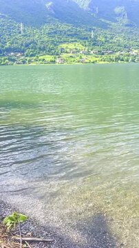 Stunning landscape featuring a calm lake reflecting the cloudy sky. Majestic mountains rise in the distance, framed by lush greenery, creating a tranquil and picturesque scene. Lake Idro, Crone, Italy