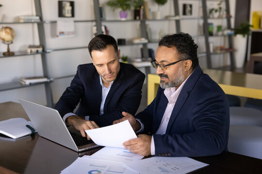 Two businessmen examining printed charts and financial data in office