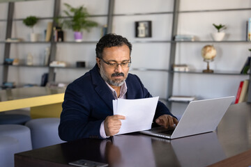 Professional man comparing information on paper with data on laptop