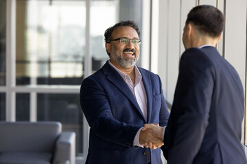 Two businessmen diverse shaking hands in workspace hallway