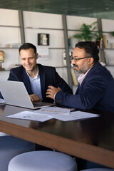 Two businessmen discussing business performance data displayed on laptop