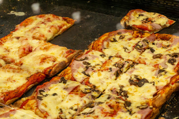 Rectangular pizza with ham, mushrooms and melted cheese served on a baking tray, freshly baked.