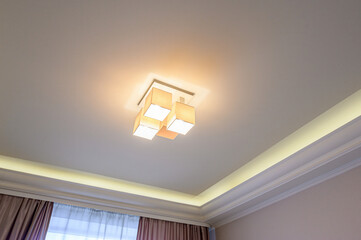 Ceiling with a modern cube-shaped light fixture and decorative molding with built-in lighting © evgeniykleymenov