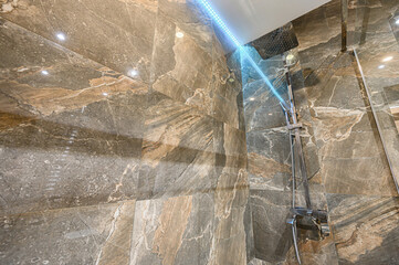 modern shower with marble-patterned tiles, stainless steel fixtures, and subtle blue LED lighting