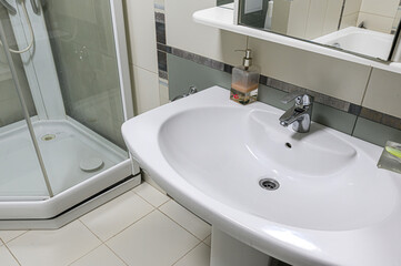 A clean, well-lit bathroom featuring a white sink, faucet, soap dispenser, and a shower cabin with a glass door.