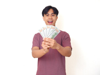Excited young man smiling while holding cash money in hand with surprised expression, isolated on...