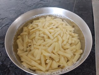 The image shows raw, cut potatoes soaking in water, which is a common preparation step for making French fries. 