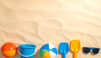 Beach toys including a ball, bucket, shovel, and sunglasses are arranged on the sand.
