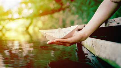 A boy from the palm of his hand lowers a paper boat into the water