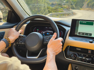 Hands firmly grip steering wheel while driving along a winding country road