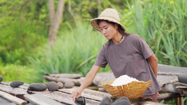 farmer harvesting natural crystalized sea salt from coconut trunks in bali indonesia, traditional hat, slow motion