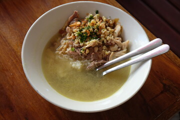 Chicken soto in a white bowl on a wooden table. Indonesian food. soto ayam Kediri. turmeric chicken clear soup.