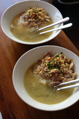 Chicken soto in a white bowl on a wooden table. Indonesian food. soto ayam Kediri. turmeric chicken clear soup.