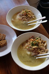 Chicken soto in a white bowl on a wooden table. Indonesian food. soto ayam Kediri. turmeric chicken clear soup. Fried tempeh in white plate. 