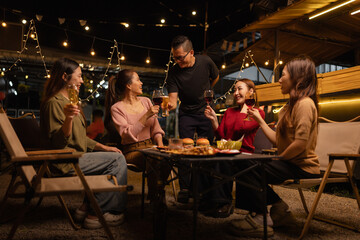 Naklejka premium Happy Friends Celebrating Together at Night, Young Asian Group of Friends Having Fun and Toasting Drinks Outdoors, Enjoying a Celebration Concept.
